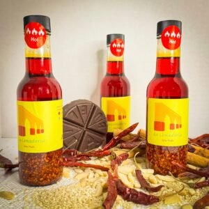 three salsa macha bottles la cenaduria brand with a chocolate bar, chilis and sesame seeds as decoration